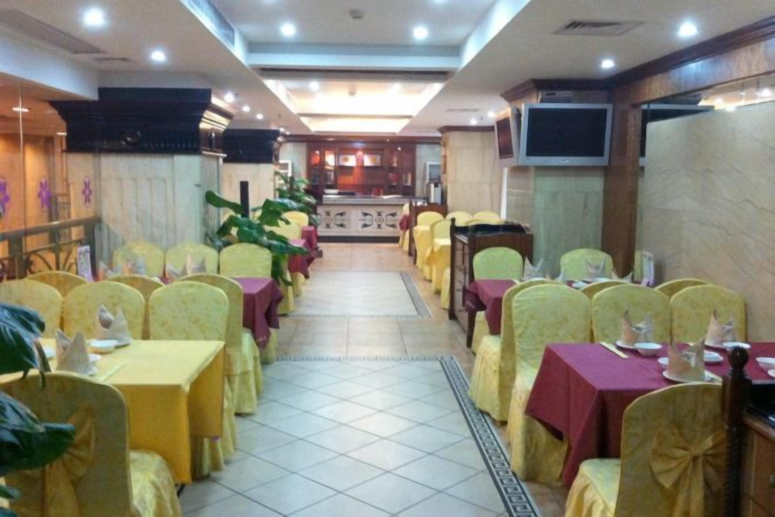 A restaurant with rows of tables and chairs, a tiled floor, and a television screen on the wall.