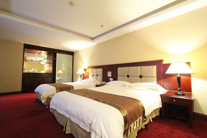 A hotel room with two beds, a red carpet, a wooden headboard, and a nightstand with a lamp.