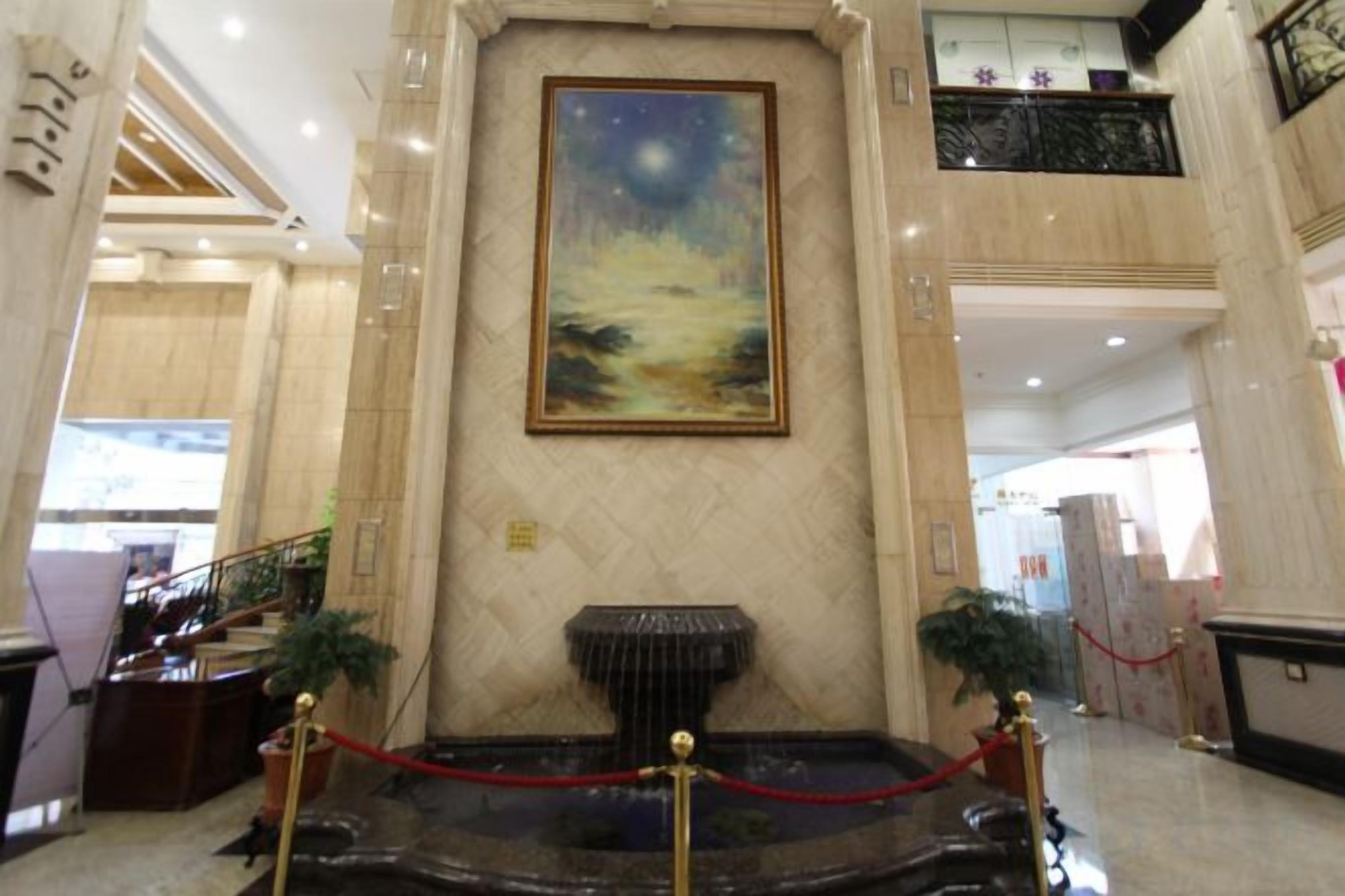A lobby with a marble reception desk, a painting above it, and a fountain in the center.
