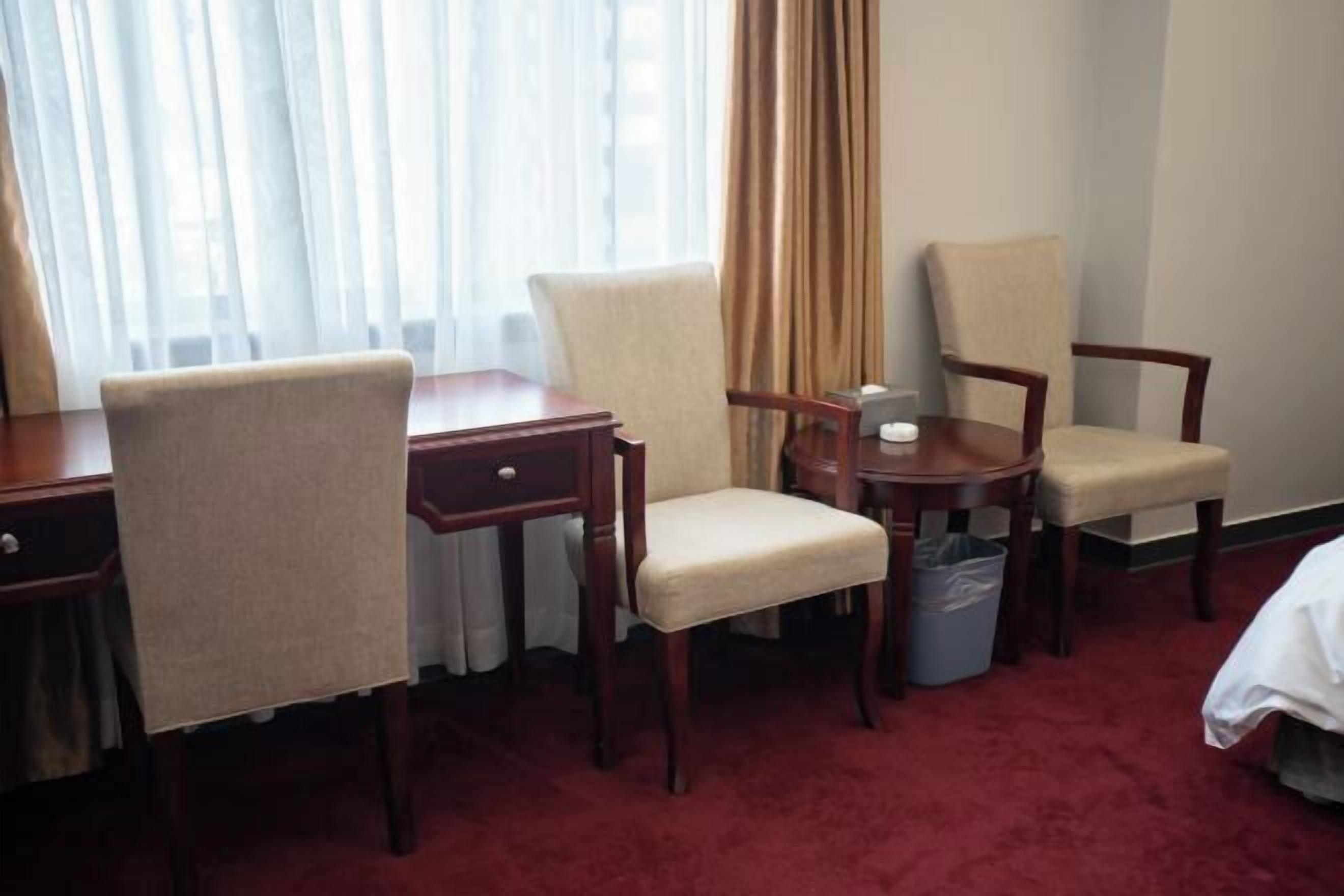 A hotel room with a desk, two chairs, a small table, a waste bin, and a bed.