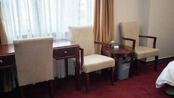 A hotel room with a desk, two chairs, a small table, a waste bin, and a bed.