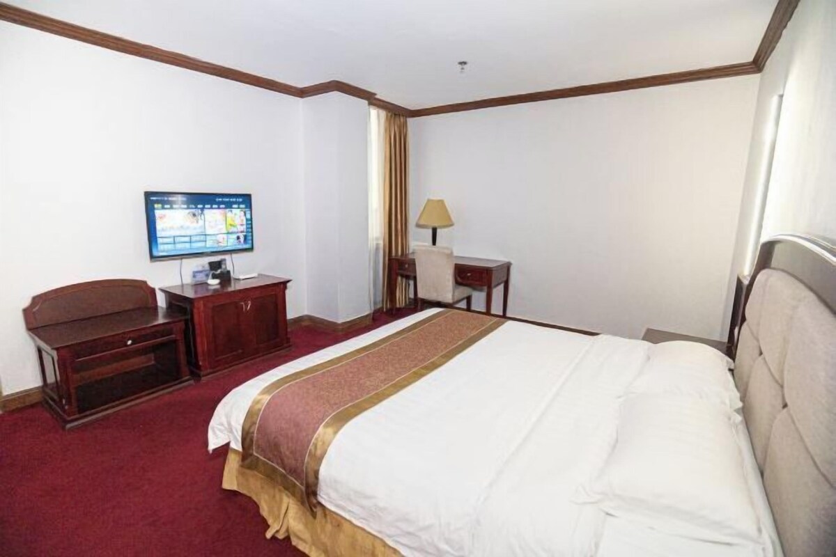 A hotel room with a large bed, a desk, a television, and a window with curtains.