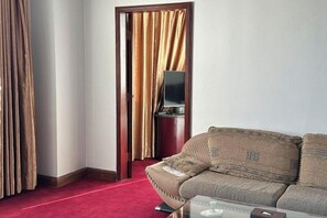A hotel room with a sofa, a television, and a red carpet.