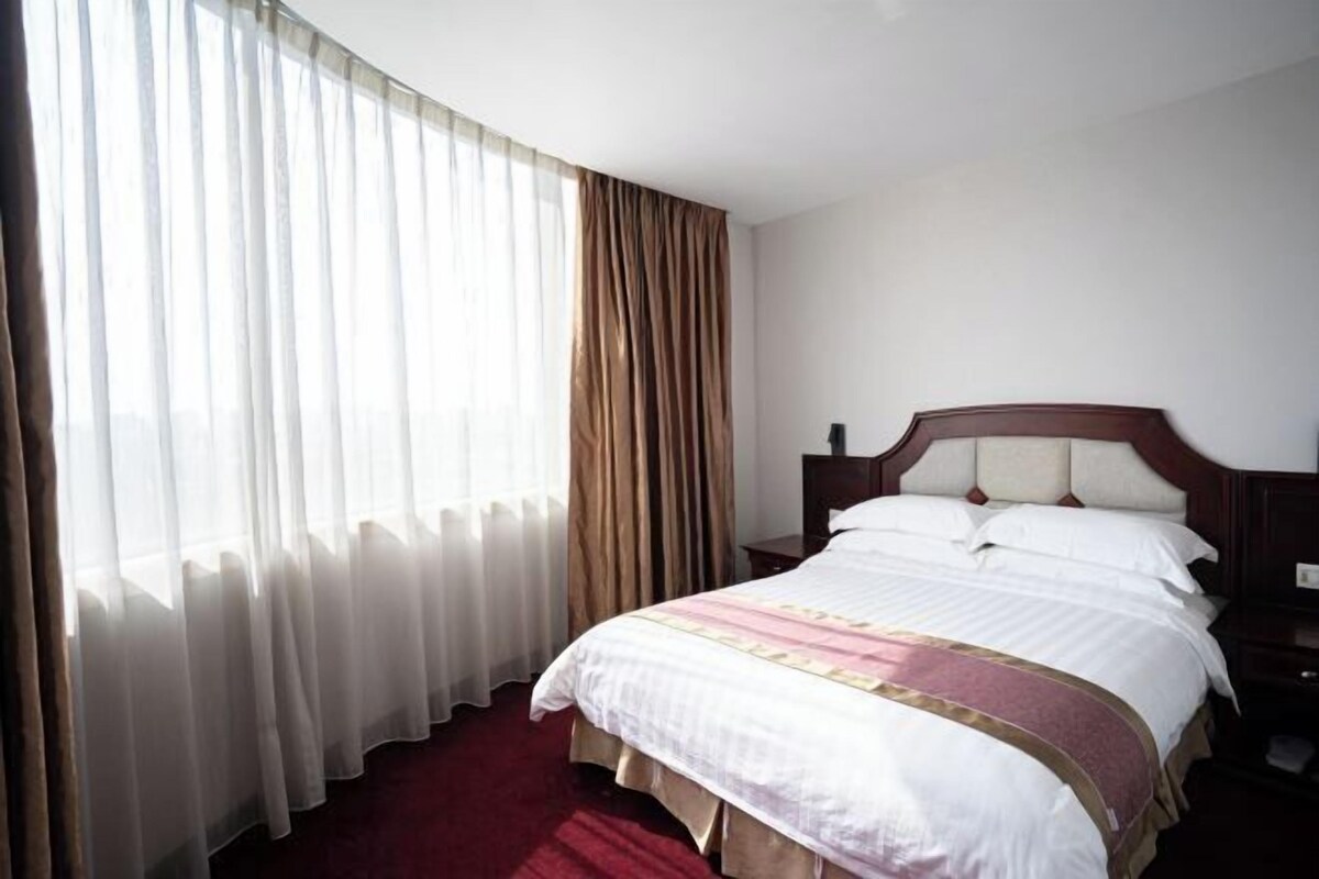 A hotel room with a bed, curtains, a nightstand, and a window.
