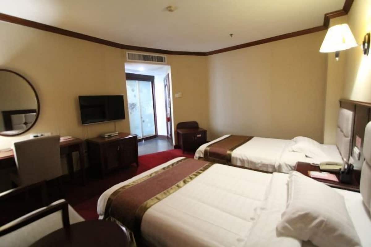 Quarto de hotel com duas camas, uma mesa, uma cadeira, uma televisão e uma luminária.
