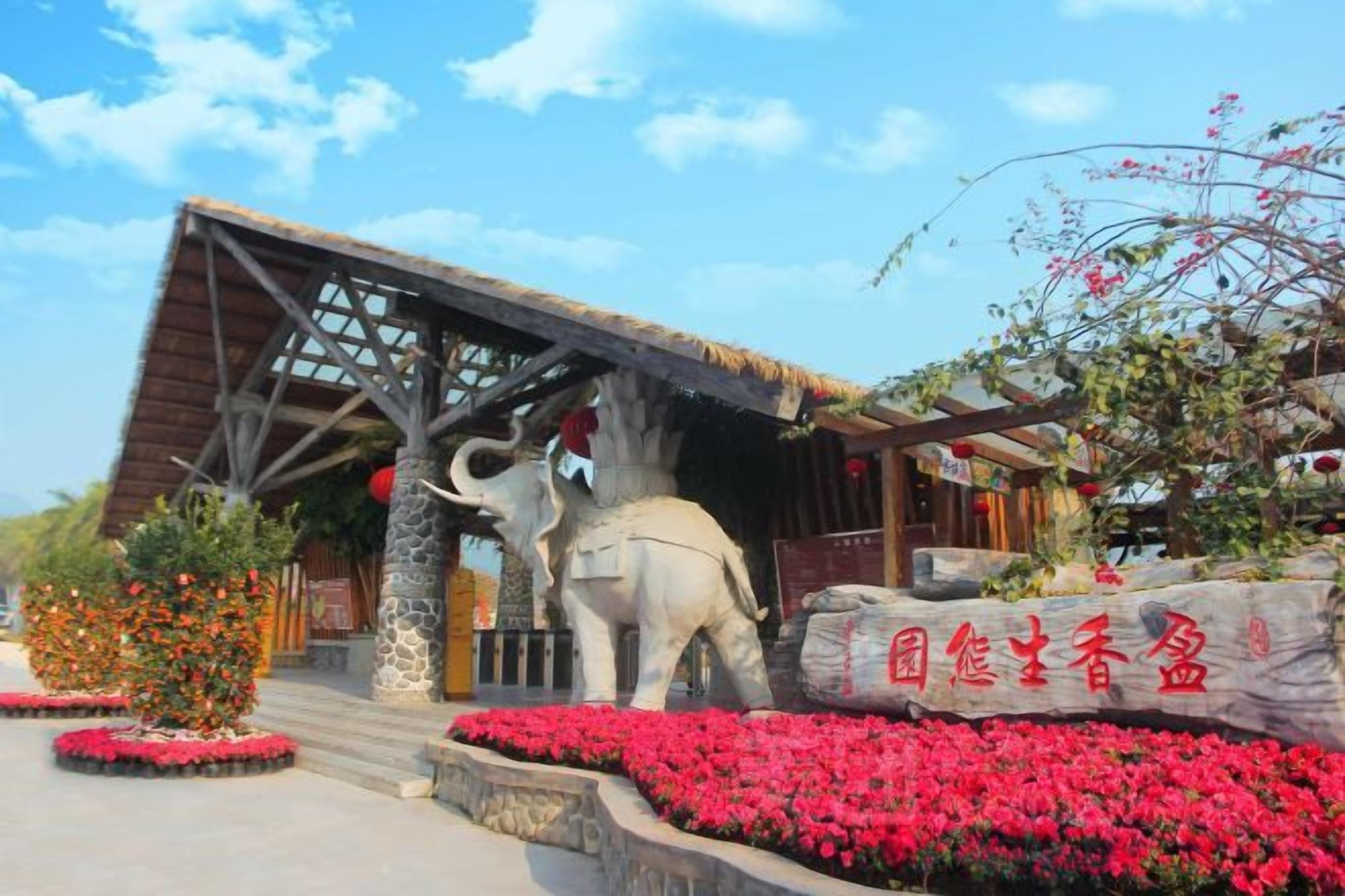 A building with a wooden structure, a large elephant statue, and red flowers.