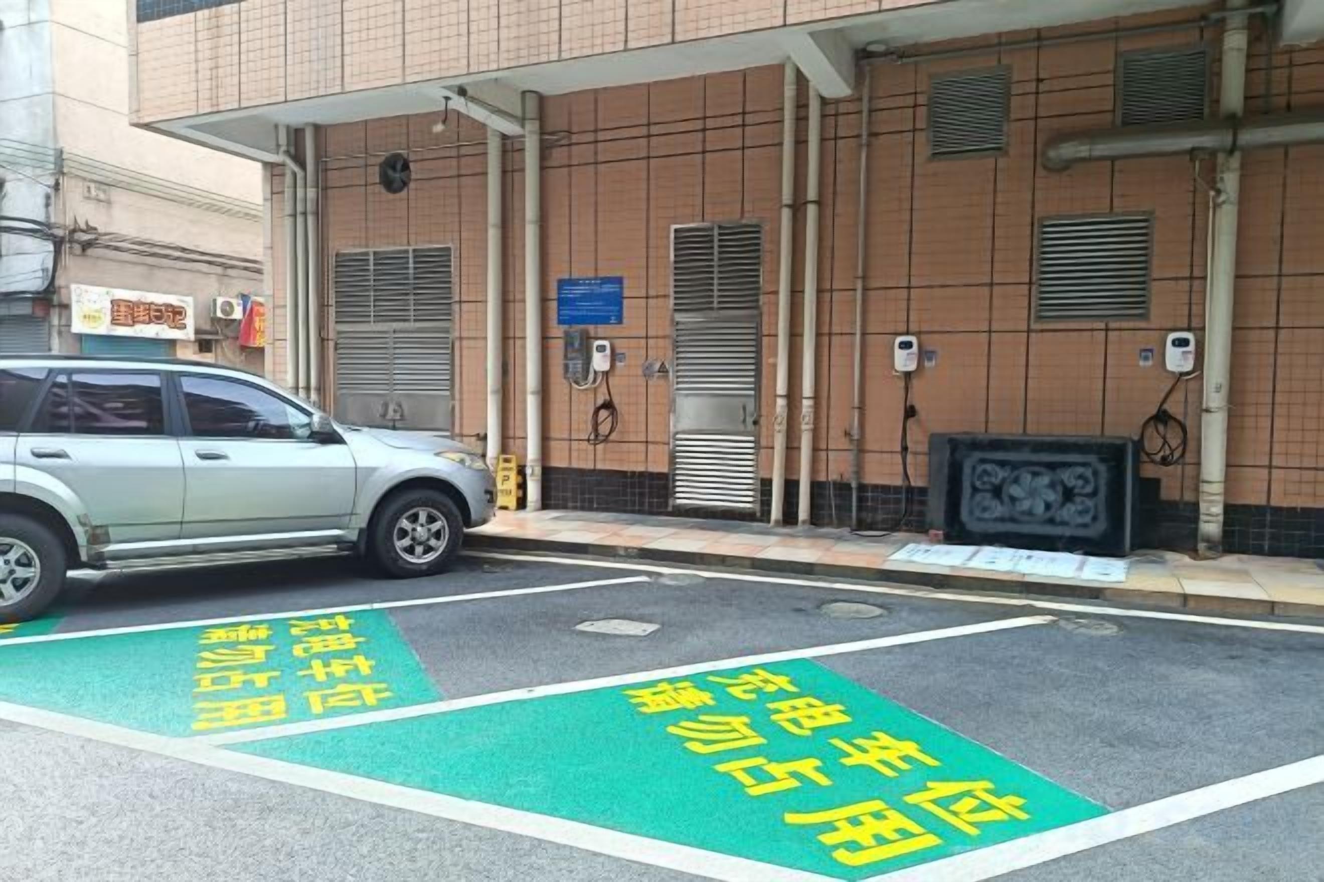 A parking area with a car parked in front of a building with a tiled facade and a signboard.