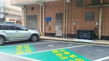 A parking area with a car parked in front of a building with a tiled facade and a signboard.