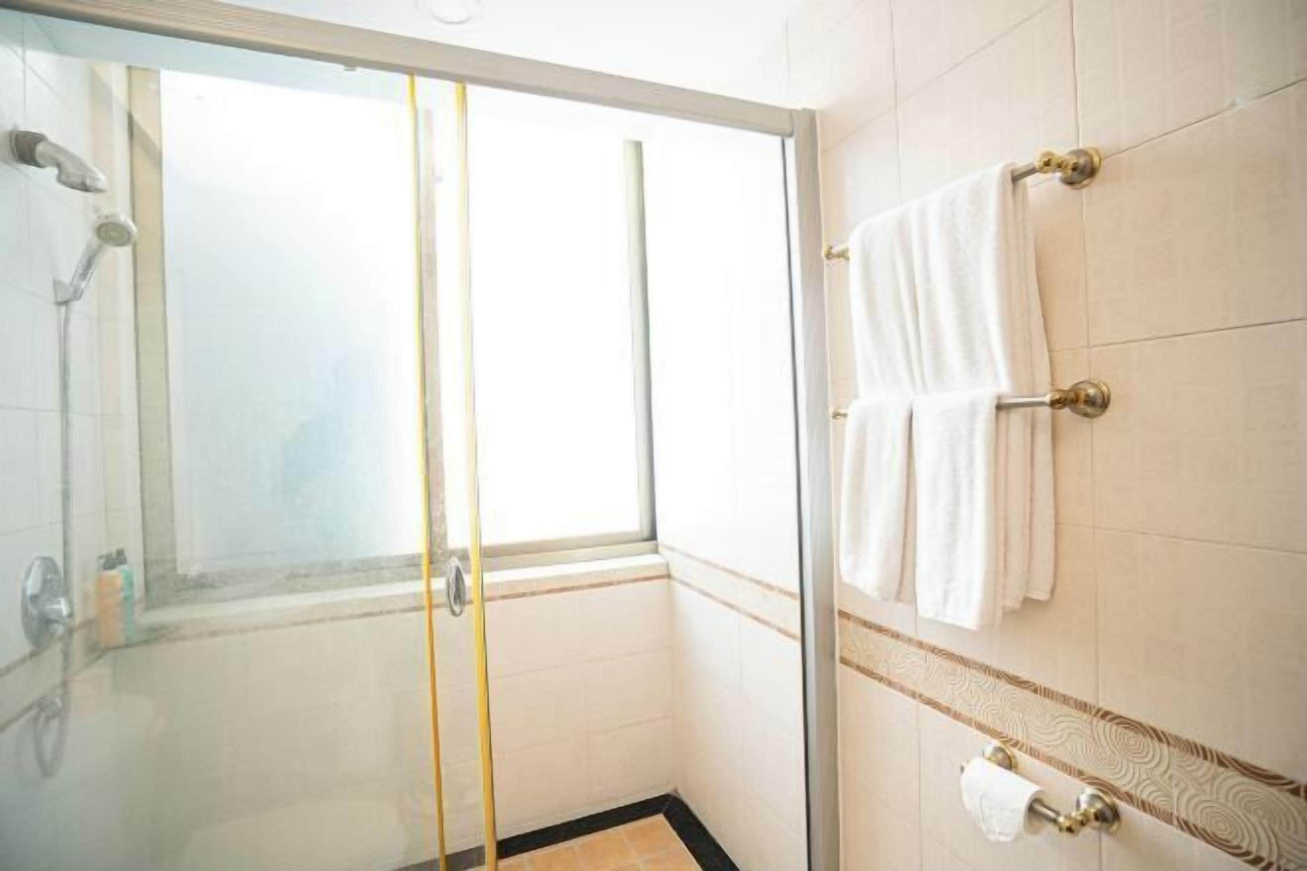 A glass-enclosed shower with a window, white tiled walls, and a towel rack with white towels.