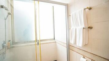 A glass-enclosed shower with a window, white tiled walls, and a towel rack with white towels.