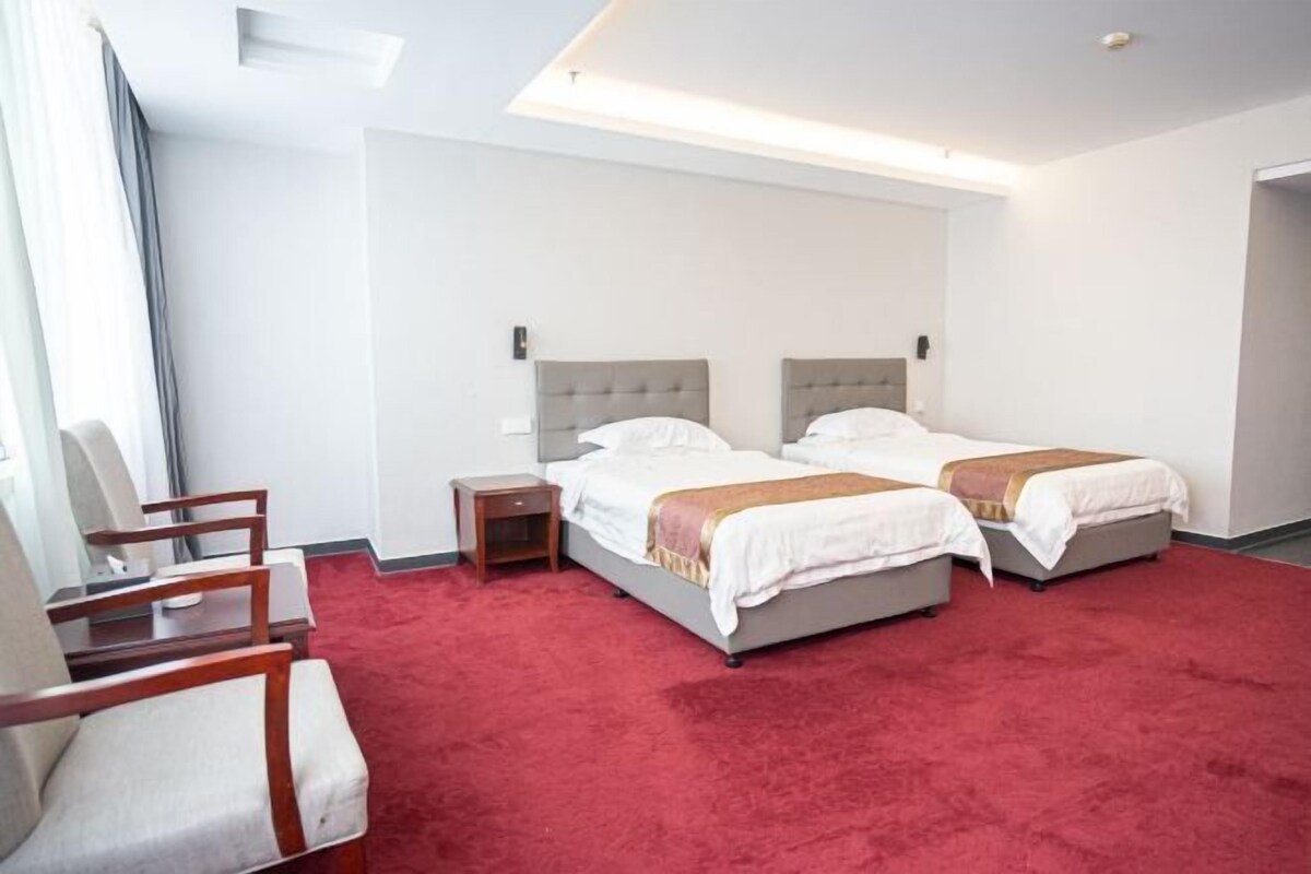 A hotel room with two beds, a red carpet, and a wooden chair.