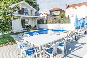 Ein Schwimmbecken mit weißer Liegefläche, umgeben von weißen Stühlen und Tischen.