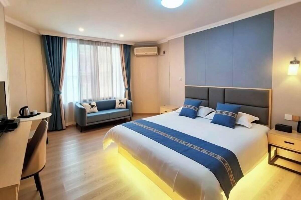 A hotel room with a large bed, a sofa, a desk, and an air conditioning unit.