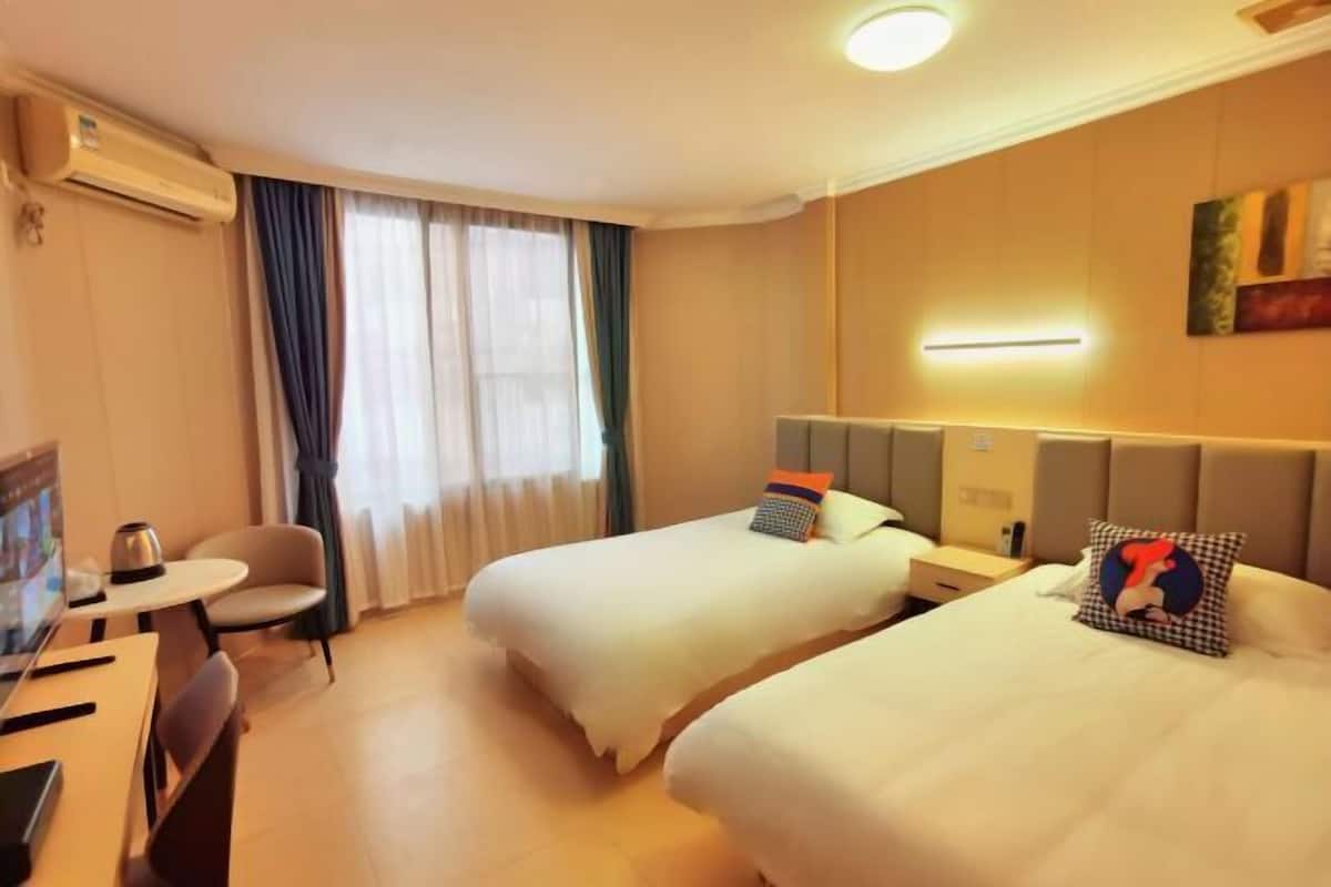 A hotel room with two beds, a desk, a chair, and a TV.