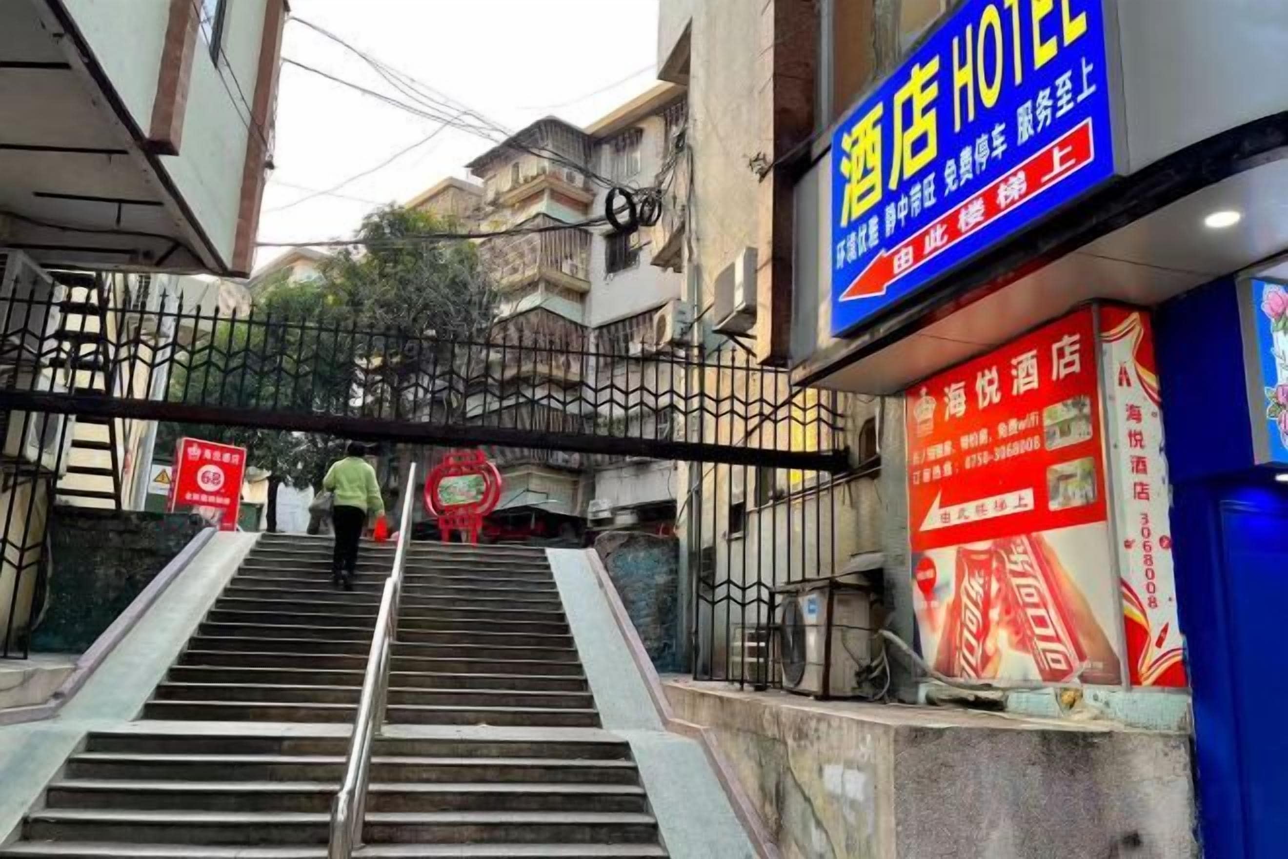 Entrada de un hotel con una escalera que sube a la puerta, un cartel sobre la entrada y un letrero rojo a la izquierda.