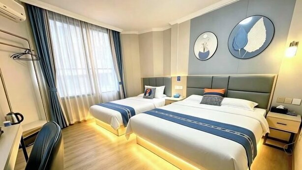 Une chambre d’hôtel avec deux lits, un bureau, une chaise et une fenêtre avec des rideaux.