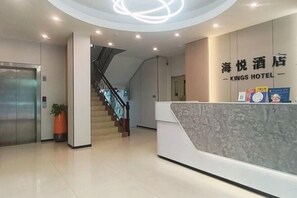 A hotel reception area with a modern design, a reception desk, a staircase, and an elevator.