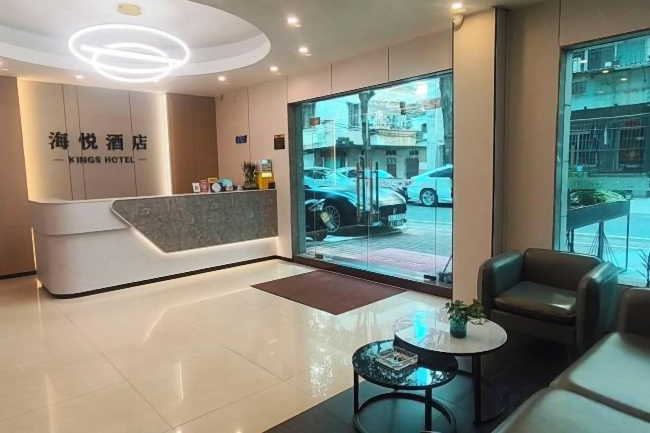A hotel reception area with a modern design, a reception desk, seating area, and a view of the street outside.