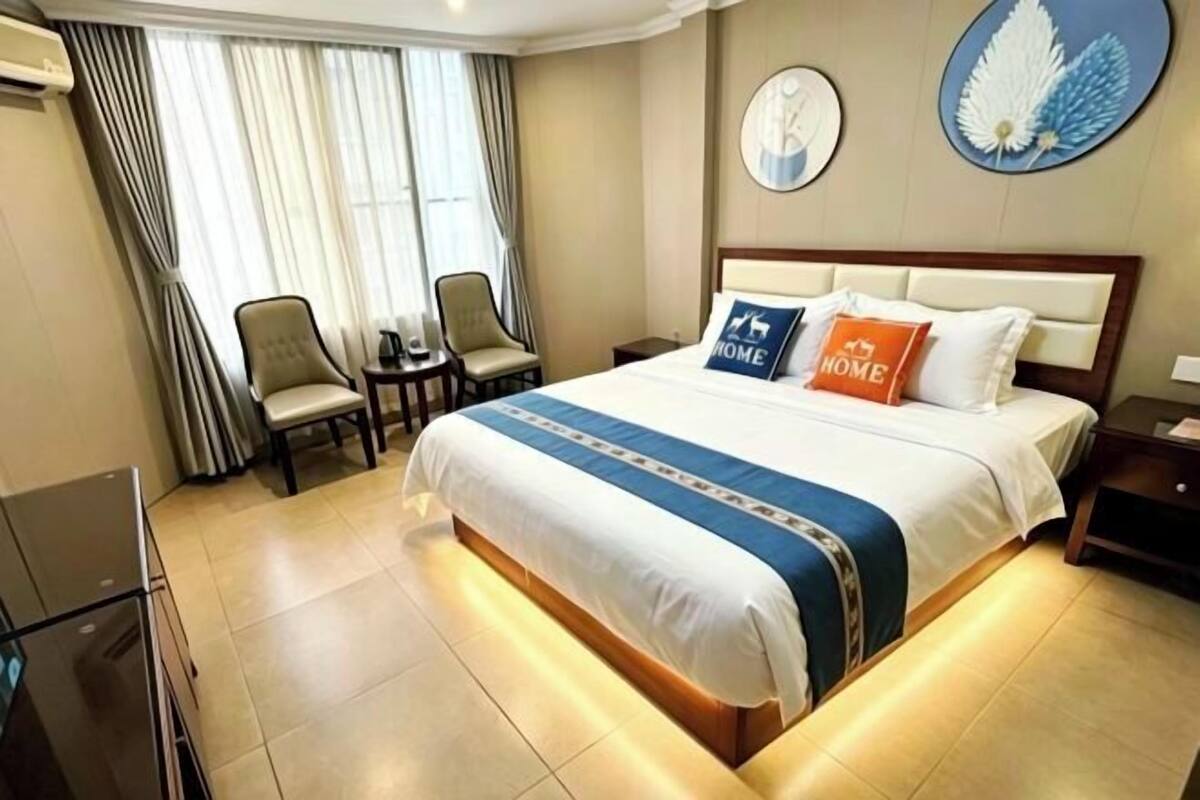 A hotel room with a large bed, two chairs, a small table, and a TV.