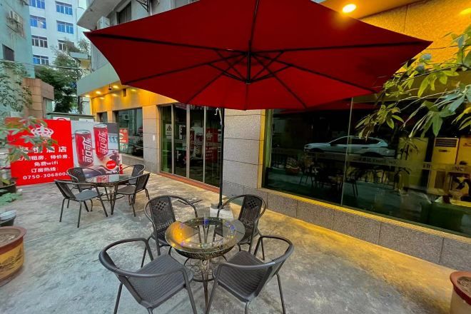 An outdoor seating area with a red umbrella, wicker chairs, and a glass table.