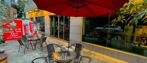 An outdoor seating area with a red umbrella, wicker chairs, and a glass table.