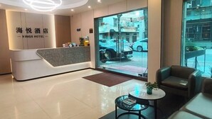 Un espace d’accueil d’hôtel au design moderne, comprenant un comptoir d’accueil, un coin salon et de grandes fenêtres donnant sur la rue.