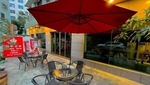 Un espace extérieur aménagé avec des tables et des chaises en verre, ainsi qu’un parasol rouge.