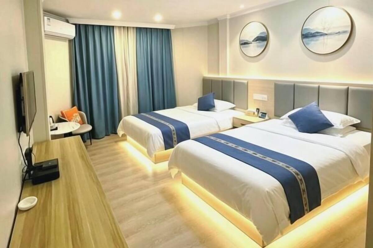 A hotel room with two beds, a desk, a TV, and a view of the outdoors.