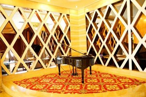 Un piano de cola en una habitación con alfombra estampada y un panel blanco geométrico.