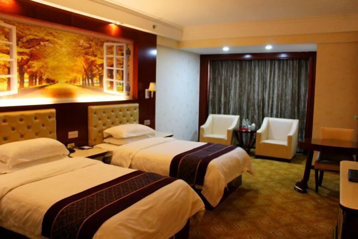 A hotel room with two beds, a painting of a tree-lined street, a large window with curtains, and a small table with chairs.
