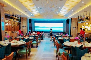 Un restaurante con varias mesas y sillas, una pantalla grande que muestra una vista panorámica y un diseño de techo moderno.