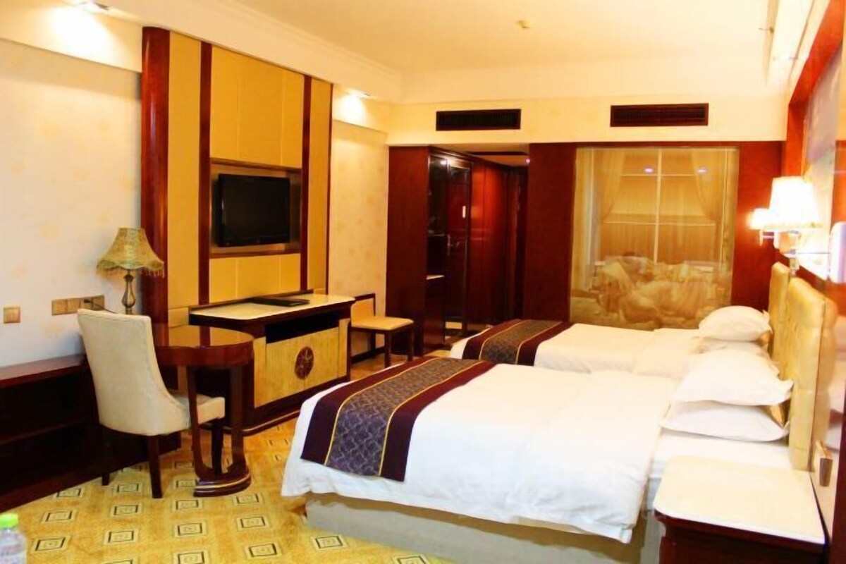 A hotel room with two beds, a desk, a chair, a television, and a window with curtains.