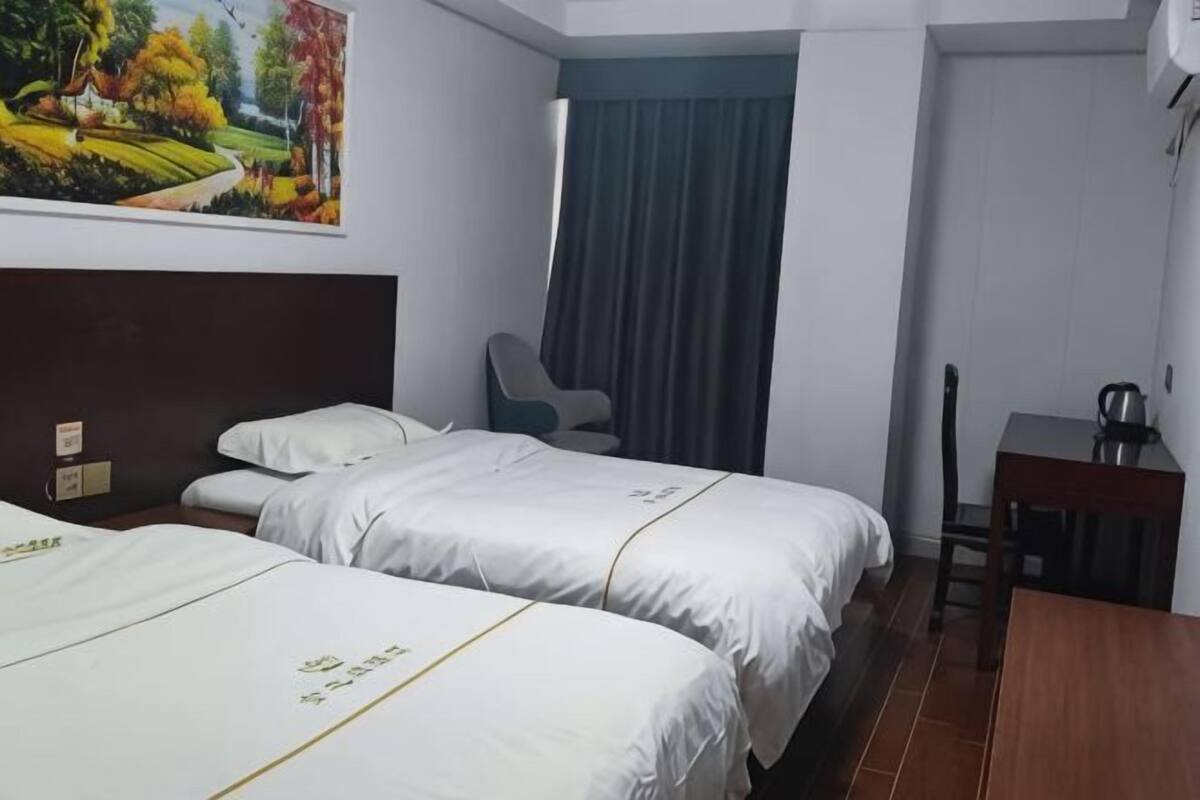 A hotel room with two beds, a desk, a chair, a painting on the wall, and a window with curtains.