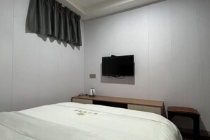 Een hotelkamer met een bed, een flatscreen televisie aan de muur, een nachtkastje met een waterkoker en een klein houten krukje.