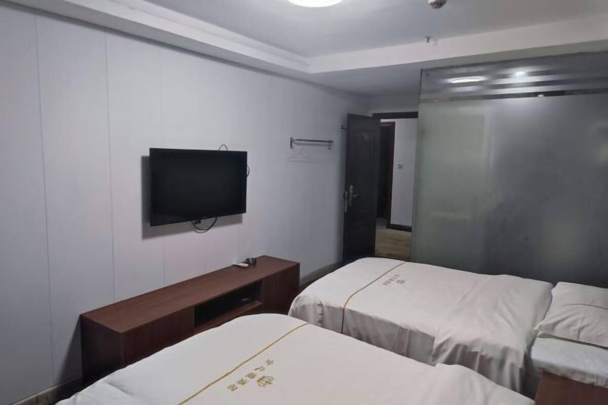 A hotel room with two beds, a TV, a wooden bench, and a wardrobe.