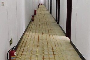 A long hallway with a fire extinguisher on the left, doors on both sides, and a tiled floor. - Jinzhiyuan Hostel (Shenzhen)