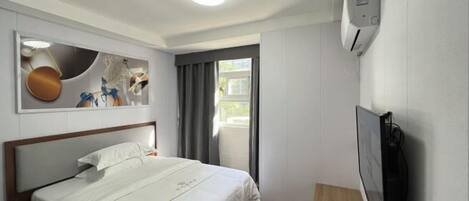 Habitación de hotel con cama, televisor, aire acondicionado instalado en la pared y ventana con cortinas.