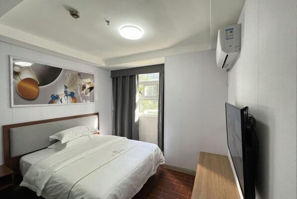 A hotel room with a bed, a TV, a wall-mounted air conditioner, and a window with curtains.