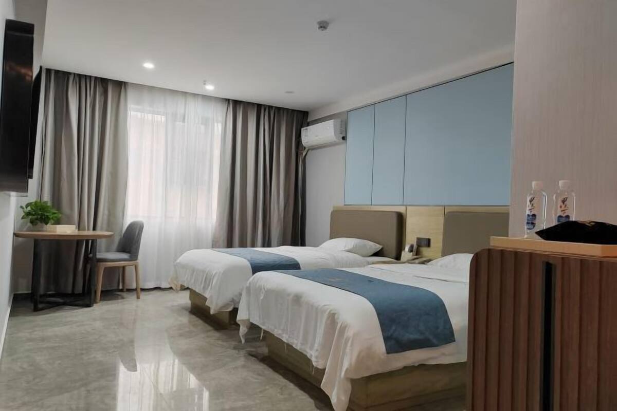 A hotel room with two beds, a desk, a chair, and a TV.