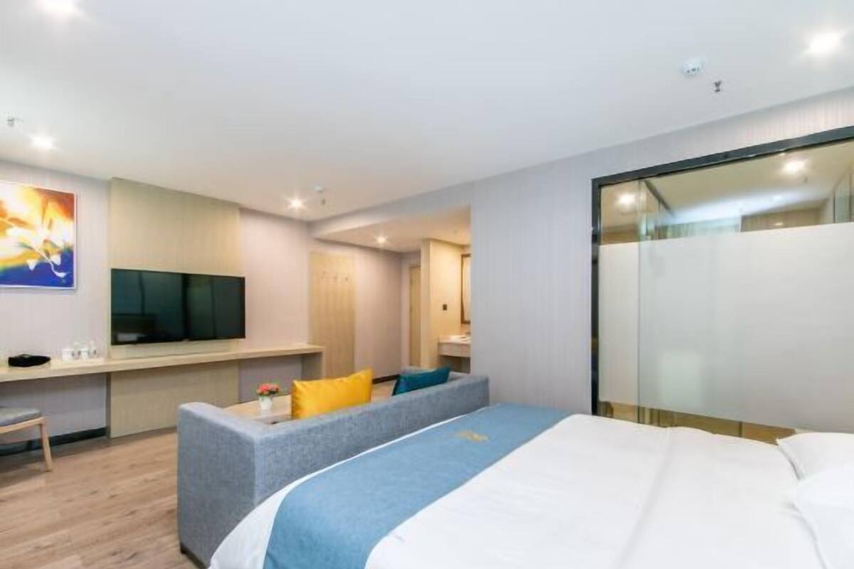 A modern hotel room with a bed, a sofa, a TV, and a desk.