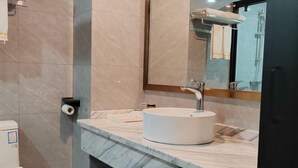 A bathroom with a marble countertop, a white sink, a mirror, and a toilet. - Oukaihua Hotel (Guilin)