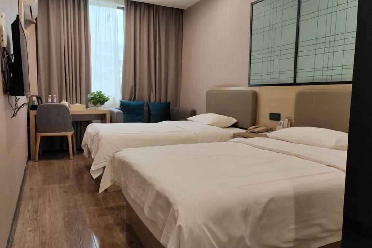 A hotel room with two beds, a desk, a chair, a TV, and a large window with curtains.
