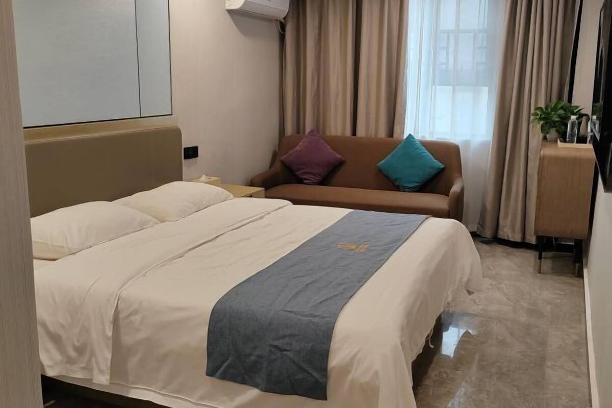 A hotel room with a bed, a sofa, a TV, and a window with curtains.