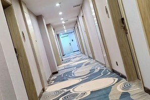 A hotel hallway with a patterned carpet, doors on both sides, and a light-colored wall. - Oukaihua Hotel (Guanyang)