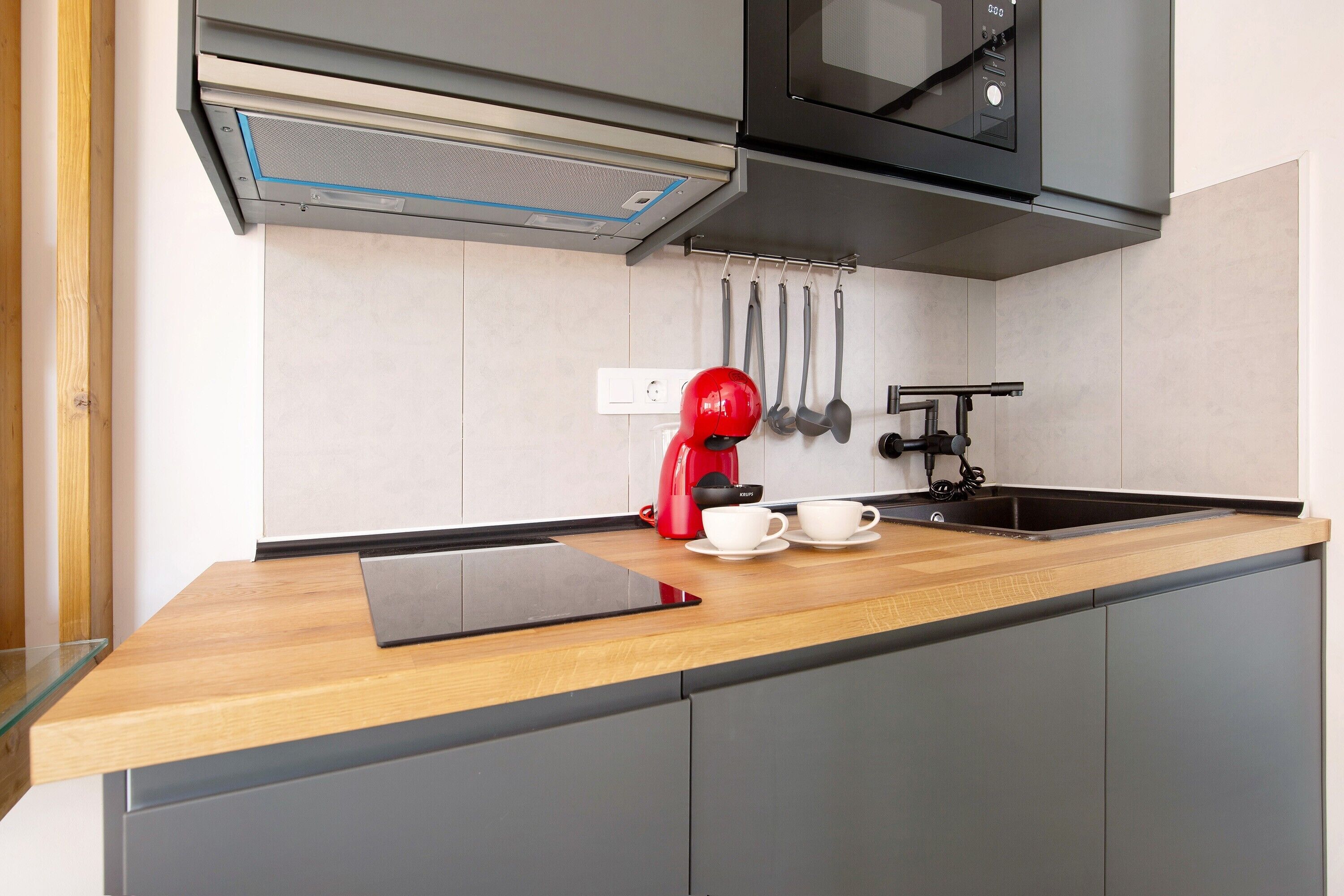 A modern kitchen with a wooden countertop, a black microwave, a red coffee maker, and a sink.