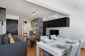 A modern living room with a sofa, a dining table set for four, and a kitchen in the background.