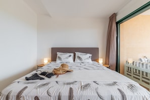 A neatly made bed with a feather pattern, a hat, and a handbag on it. There are two bedside lamps and a nightstand with a lamp. - Apartment 'Altea La Nova' with Shared Pool & Wi-Fi (Altea la Vella)