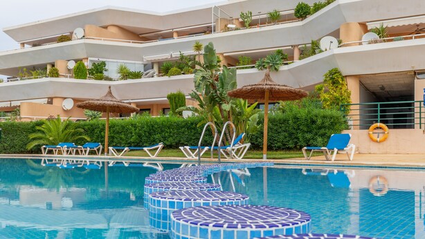Piscina com degraus azulejados em azul e branco, espreguiçadeiras e guarda-sóis.