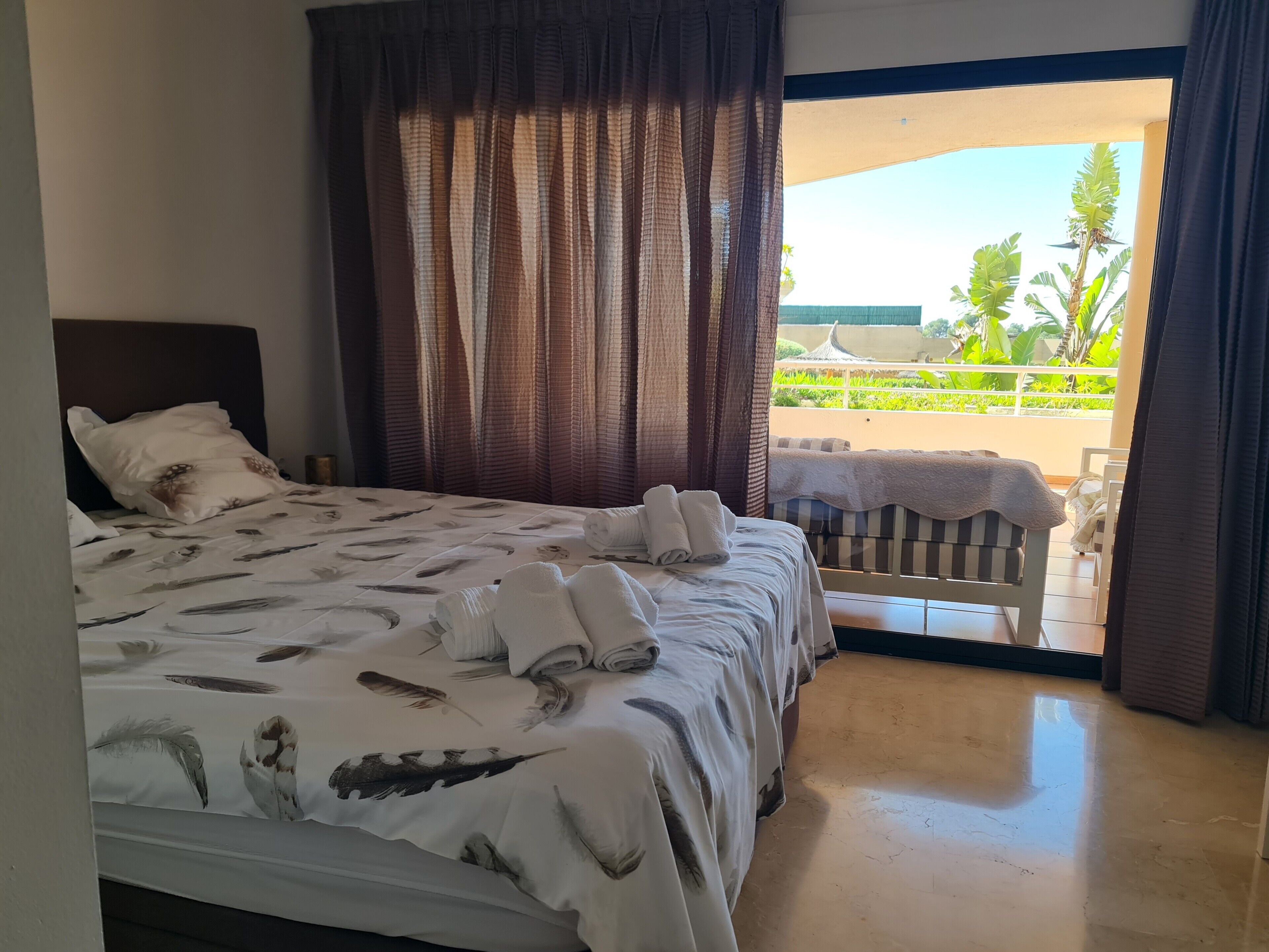 Une chambre d’hôtel avec un lit, des rideaux, une vue sur l’extérieur et un balcon.
