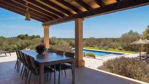 A covered outdoor area with a pool, a table with chairs, and a view of the landscape.